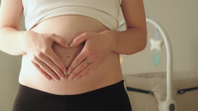 Pregnant woman forming a heart with her hands on the belly, closeup shot