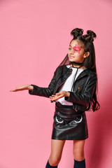 Little - fashionable hipster punk girl - dressed in a leather jacket and skirt, black knee-highs and a white T-shirt, with a funny hairstyle and a makeup star on the face, points to the side
