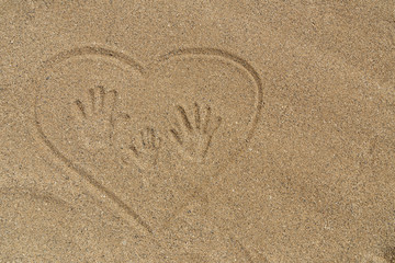 Fototapeta na wymiar Family vacations. Mom's, Dad's and child's handprints trace on the sand in heart.