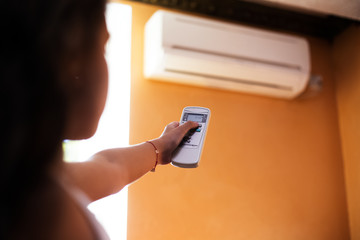 Close-up of child hand adjusting air conditioner with remote control on orange background.