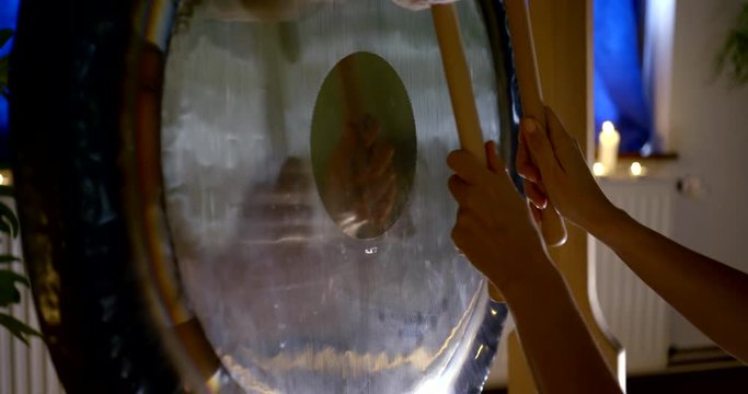 closeup view of bronze gong and two mallets in hands of woman in room