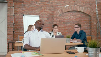 Tired Male African Startup Worker has Backache, Suffering from Back Pain after Long Sitting at Work with Laptop in Modern Loft Office. 4K Static Medium Shot