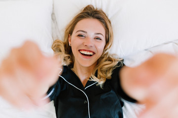 Naklejka premium Above frame of happy laughing european woman lying on white pillow and making selfie in the morning at home