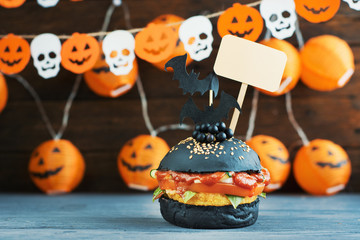 Halloween Spooky Black Burger with Cheese. Cheeseburger on Halloween pumpkin head jack lantern background