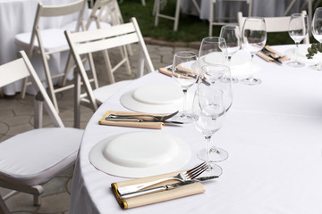 Wedding table setting decorated with fresh flowers in a brass vase. Wedding floristry. Banquet table for guests outdoors with a view of green nature. Bouquet with roses, eustoma and eucalyptus leaves