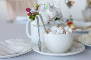 A Cup filled with lump sugar with tongs on a white tablecloth