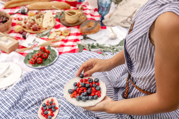 Woman in checkered stylish dress take berry from berries plate. Outdoor picnic © Kate