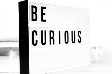Be curious quote on a wooden white background. Motivational business start up board