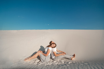 Romantic pair sit on white sand and huggins, in desert.