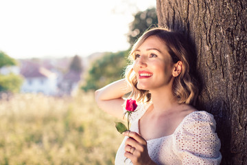 Beautiful blond lady in white dress with rose in the garden