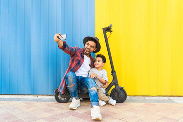 Young Father Taking a Selfie with his Son on an Electric Scooter.