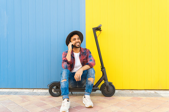 Latin Young Man Having a Phone Call While Sitting on Electric Scooter.