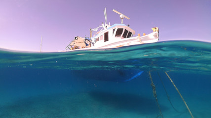 Above and below underwater photo of colourful traditional fishing boat docked in crystal clear...