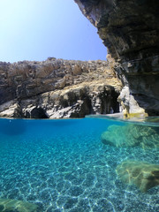 Above and below underwater photo of crystal clear sea paradise rocky seascape full of caves beach...