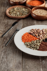 white plate with lentil, pumpkin seeds and beans near knife and fork on wooden table