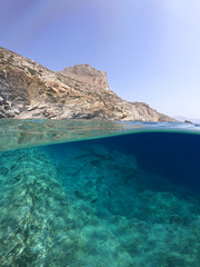 Above and below underwater photo of crystal clear sea paradise rocky seascape full of caves beach...
