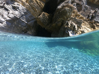 Above and below underwater photo of crystal clear sea paradise rocky seascape full of caves beach...