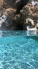 Fototapeta na wymiar Above and below underwater photo of crystal clear sea paradise rocky seascape full of caves beach of Mouros, Amorgos island, Cyclades, Greece