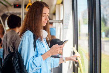 Pretty female passenger sits with smartp hone while moving in the modern tram or subway. Trip at the public transport.