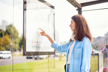 Young woman waiting for the public transport while standing at the modern tram station outdoors