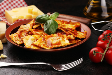 Ravioli with tomato sauce garnished with parmesan cheese and basil on rustic table