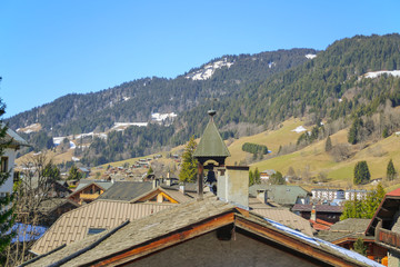 Fototapeta na wymiar Roof and bell tower of Chapel Saint Anne and alpine view in the background on a sunny day in the spring at Megeve.
