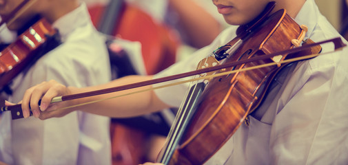 Asian boy students playing violin with music notation in the group. Violin player. Violinist hands playing violin orchestra musical instrument closeup. Symphony orchestra on stage. Selective focus. © Koonsiri