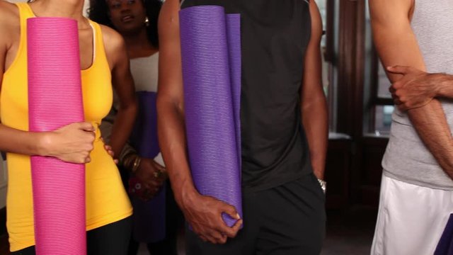 Men and women in yoga attire holding rolled up yoga mats