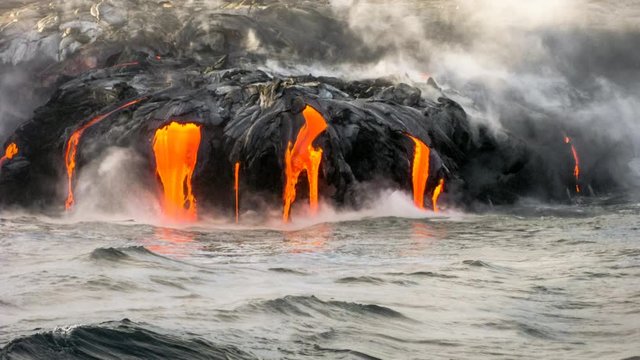 Sea view of Kilauea Volcano in Big Island, Hawaii, United States. A restless volcano that has been in business since 1983. Cinemagraph loop with lava flowing in the dark and jumping into the sea.