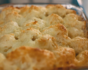 Baked cauliflower gratin in a glass bowl on a wooden table viewed from above.