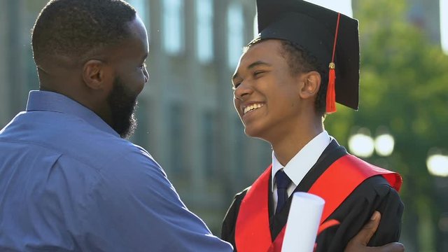 Happy black man hugging smiling son in magisterial suit, proud father, support