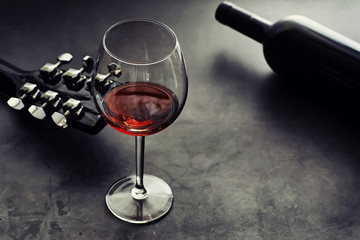 Guitar and high glass with red wine on a stone background.