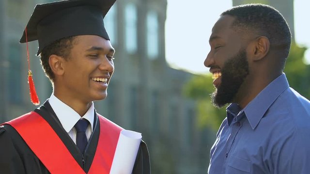 Extremely happy black father congratulating son in magisterial suit, graduation