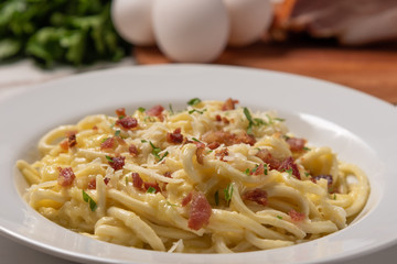 Carbonara pasta with pancetta, egg, hard parmesan cheese and cream sauce.  White plate on white wooden background. Traditional italian cuisine. Pasta alla carbonara