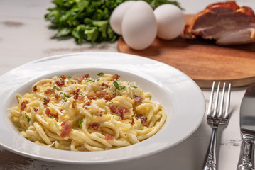 Carbonara pasta with pancetta, egg, hard parmesan cheese and cream sauce.  White plate on white wooden background. Traditional italian cuisine. Pasta alla carbonara