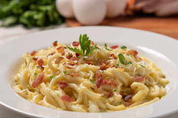 Carbonara pasta with pancetta, egg, hard parmesan cheese and cream sauce.  White plate on white wooden background. Traditional italian cuisine. Pasta alla carbonara