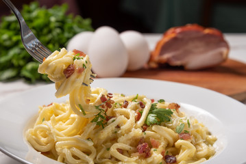 Carbonara pasta with pancetta, egg, hard parmesan cheese and cream sauce.  White plate on white wooden background. Traditional italian cuisine. Pasta alla carbonara