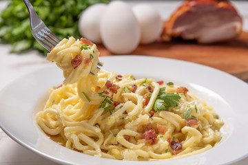 Carbonara pasta with pancetta, egg, hard parmesan cheese and cream sauce.  White plate on white wooden background. Traditional italian cuisine. Pasta alla carbonara