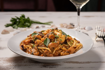 Pasta with sea fruit in white plate on a white wooden background, soft light. Spaghetti ai frutti di mare, seafood mediterranean gastronomy