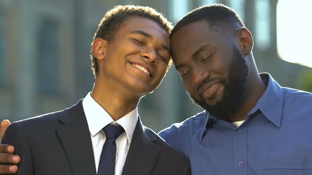 Proud black male hugging teenage boy feeling happy, family support and trust