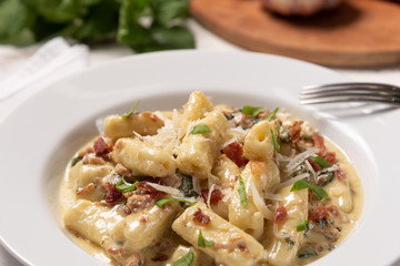 Penne pasta with carbonara sauce in white plate on wooden white background, soft light, angle view. Italian food