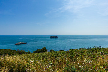 A panorama seascape view with rocky islands along the coast under a majestic blue sky and some white clouds