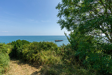 Fototapeta premium A panorama seascape view with rocky island along the coast under a majestic blue sky and some white clouds