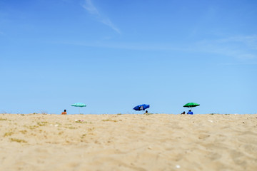 Wide angle view on tourists on the sand beach under the sunshade parasol umbrella against a blue sky in sunny day vacation