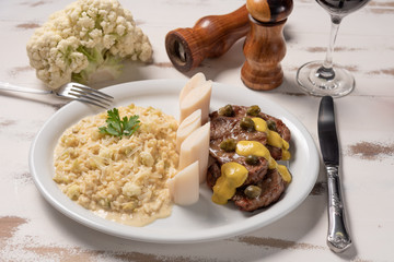 Risotto with filet mignon. Risoto and beef with capers and mustard in a white plate on wooden white background. Soft light. Italian food.