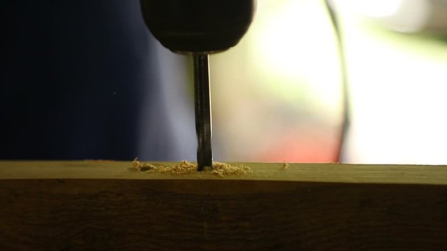 A carpenter drills a hole in a board with an electric drill, outdoors, close-up