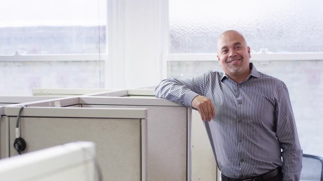 Smiling Hispanic businessman leaning on cubicle wall