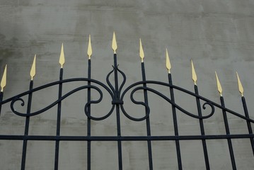 part of an iron fence with sharp black bars against a gray concrete wall