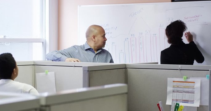 Business people talking in meeting at cubicles with whiteboard