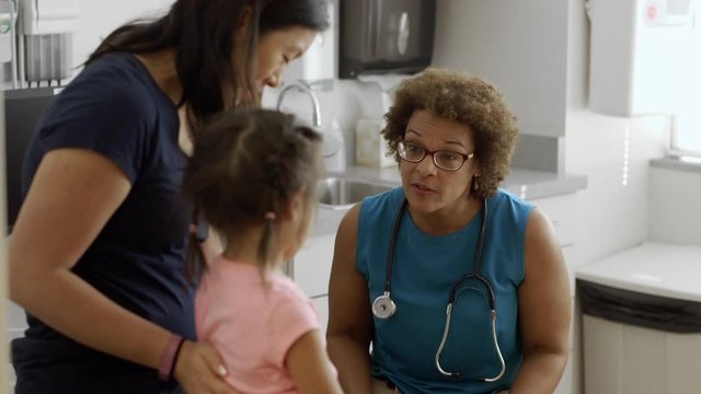 Pediatrician talking to mother and daughter in examination room